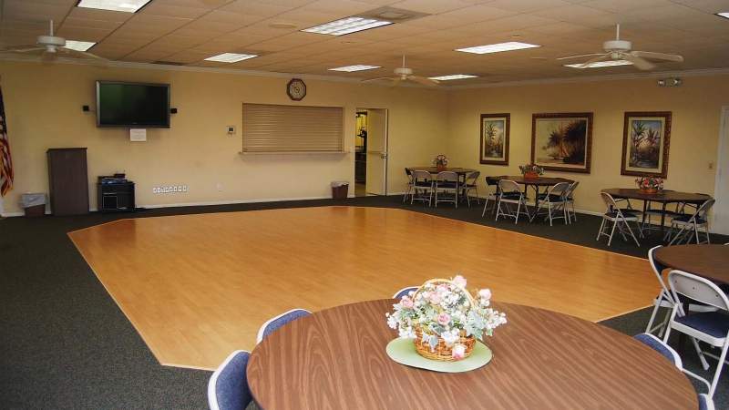 012 - Vista Plantation clubhouse interior of a meeting room with tables, chairs, and floral centerpieces featuring a TV, clock, and wall decorations_