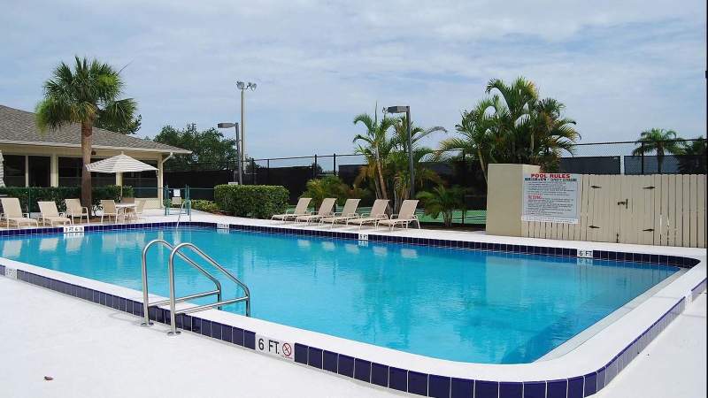 013 - A Vista Plantation community swimming pool with deck chairs, a 6-foot depth marker, and tropical plants under a cloudy sky_