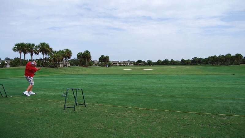 015 - A golfer in red and white clothing swings a club on a green golf course under a cloudy sky_