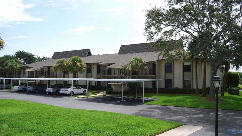 021 - A Vista Plantation complex with covered parking spaces under a clear sky, surrounded by lush green trees_