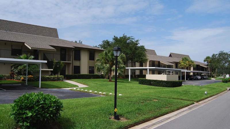 024 - A Vista Plantation street with two-story homes featuring brown roofs and covered parking, landscaped with green grass and shrubs under a partly cloudy sky_