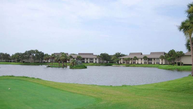 031 - A scenic view of a Vista Plantation golf course with a pond in the foreground, surrounded by residential buildings under a cloudy sky_